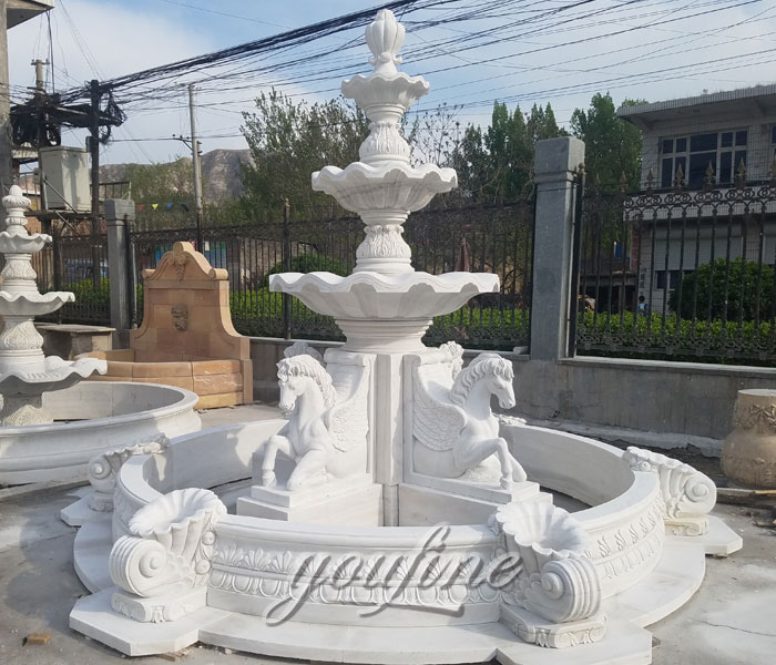 Large outdoor white tiered water fountains with  horse statues in the front of hotel